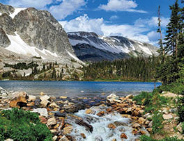 A mountain stream flows through a valley with a lake nearby. The stream is surrounded by rocks and trees, creating a serene and natural setting. AI generated content