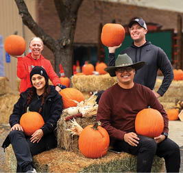 Four people are sitting on a pile of hay, holding pumpkins. AI generated content